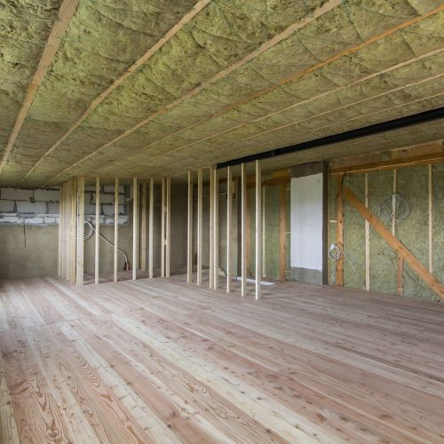 Construction and renovation of big spacious empty unfinished attic room with oak floor, walls and ceiling insulated with rock wool and fiber glass for cold barrier and wooden frame for future walls.